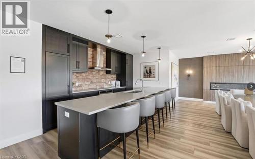 Open-concept kitchen and dining area featuring a lengthy island with seating, dark cabinetry, a brick-patterned backsplash, and wood-finish flooring - 50 Grand Avenue S Unit# 713, Cambridge, ON - Indoor Photo Showing Kitchen With Upgraded Kitchen