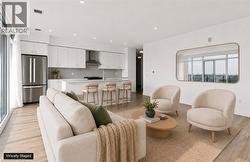 Open-concept living space featuring wood-finish flooring, recessed lighting, and a white kitchen with stainless steel appliances - 