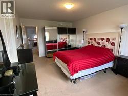 Carpeted bedroom featuring a light-colored headboard, a ceiling-mounted light fixture, and a doorway leading to a hallway with a wooden railing - 