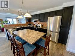 Kitchen featuring dark wood cabinetry, stainless steel appliances, a mosaic tile backsplash, a central island with a durable countertop, and wood-finish flooring - 