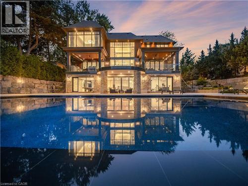 Multi-level property featuring stone and stucco exterior, extensive glass paneling, and multiple balconies with glass railings - 140 Secord Lane, Burlington, ON - Outdoor With In Ground Pool
