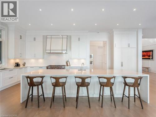 Contemporary kitchen featuring an oversized island with seating, white shaker-style cabinetry, integrated stainless steel appliances, recessed ceiling lighting, and light wood-finish flooring - 140 Secord Lane, Burlington, ON - Indoor Photo Showing Kitchen With Upgraded Kitchen