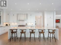 Contemporary kitchen featuring an oversized island with seating, white shaker-style cabinetry, integrated stainless steel appliances, recessed ceiling lighting, and light wood-finish flooring - 