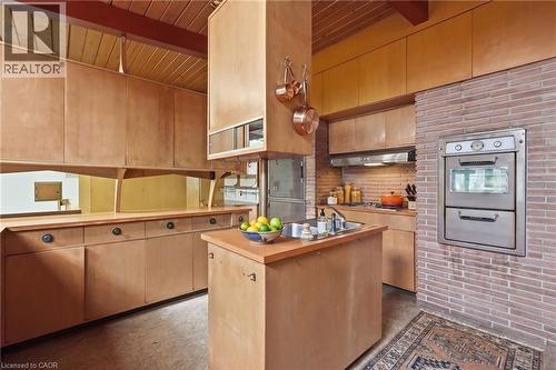 Virtually Staged - Kitchen featuring extensive wood cabinetry, a built-in stainless steel double oven, a natural brick accent wall, and a wood-paneled ceiling with exposed beams - 264 Mountain Brow Boulevard, Hamilton, ON - Indoor Photo Showing Kitchen