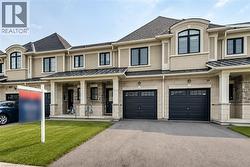 Contemporary townhome facade featuring a neutral stucco and stone material mix, dark-framed windows, individual garages with panel designs, a covered entry porch, and a paved driveway - 
