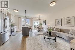 Open-concept living area featuring wood-finish flooring throughout, a modern kitchen with stainless steel appliances, a central island with seating, a dining area with chandelier lighting, and abundan - 