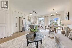 Open-concept living space featuring wood-finish flooring, a contemporary kitchen with stainless steel appliances, an eat-in island, and an adjacent dining area with a modern chandelier - 