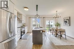 Open-concept kitchen and dining area featuring wood-finish flooring, white cabinetry, stainless steel appliances, a center island with seating, and a sliding glass door to the exterior - 