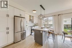 Modern kitchen featuring white cabinetry, stainless steel appliances, a center island with a sink, quartz countertops, and wood-finish flooring - 