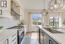 Modern kitchen featuring light wood-finish flooring, white cabinetry with black pulls, and a stainless steel range with a coordinating hood vent - 