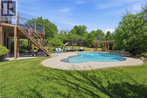 Freeform swimming pool with concrete surround, adjacent to a wooden deck with glass panel railings - 5779 Third Line, Guelph/Eramosa, ON - Outdoor With In Ground Pool With Backyard