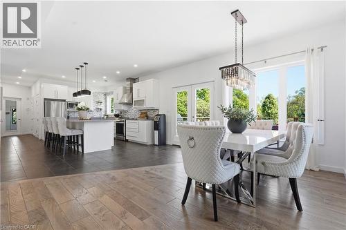 Open-concept living area featuring wood-finish flooring, a contemporary kitchen with white cabinetry and stainless steel appliances, a kitchen island with seating, and a dining area illuminated by a c - 5779 Third Line, Guelph/Eramosa, ON - Indoor Photo Showing Dining Room