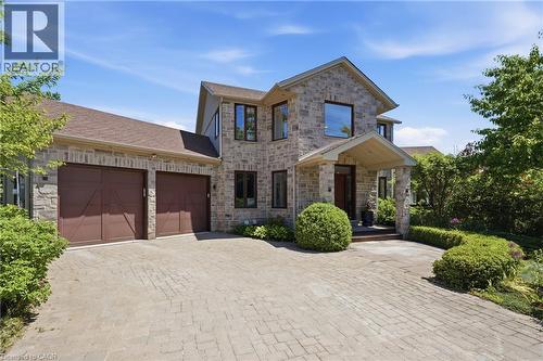Stone veneer exterior with a covered entry, dark wood front door, and a two-car garage featuring brown carriage-style doors - 5779 Third Line, Guelph/Eramosa, ON - Outdoor With Facade