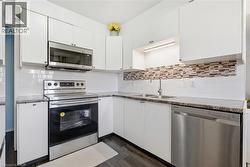 Kitchen featuring white cabinetry, stainless steel appliances, dark wood-finish flooring, and a subway tile backsplash with an accent mosaic - 