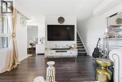 Spacious living area featuring dark wood-finish flooring, white walls, and a prominent staircase with dark treads and white risers - 