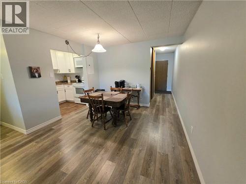 Open-concept living space featuring wood-finish flooring, a dining area with pendant lighting, and a partial view of the kitchen with white cabinetry - 24 Mooregate Crescent Unit# 103, Kitchener, ON - Indoor Photo Showing Dining Room