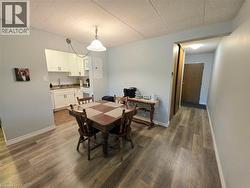 Open-concept dining area featuring wood-finish flooring, a contemporary ceiling light fixture, and a pass-through to the kitchen with white cabinetry and subway tile backsplash - 