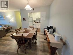 Open-concept living space with wood-finish flooring, a dining area, and a kitchen featuring white cabinetry and subway tile backsplash - 