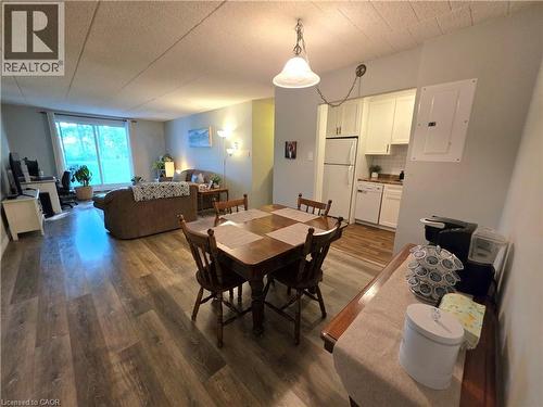 Open-concept living area featuring wood-finish flooring, a dining space with a pendant light fixture, and a kitchen with white cabinetry and appliances - 24 Mooregate Crescent Unit# 103, Kitchener, ON - Indoor Photo Showing Dining Room