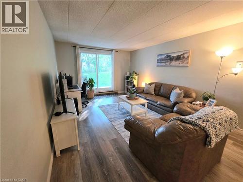 Spacious living area featuring wood-finish flooring, light-colored wall paint, and a large sliding glass door opening to a green outdoor space - 24 Mooregate Crescent Unit# 103, Kitchener, ON - Indoor Photo Showing Other Room