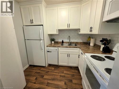 Kitchen featuring white cabinetry with dark hardware, a white subway tile backsplash, laminate countertops, and wood-finish flooring - 24 Mooregate Crescent Unit# 103, Kitchener, ON - Indoor Photo Showing Kitchen With Double Sink