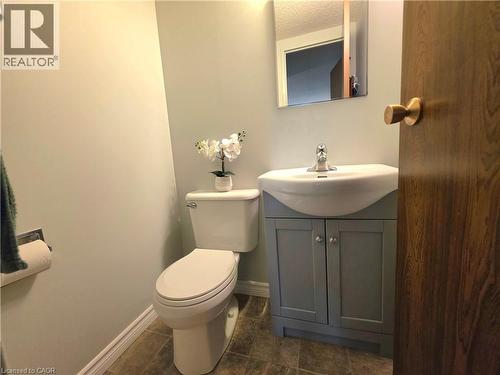 Powder room featuring a ceramic toilet, light gray walls, a gray vanity with a white integrated sink, chrome faucet, and a rectangular wall-mounted mirror - 24 Mooregate Crescent Unit# 103, Kitchener, ON - Indoor Photo Showing Bathroom