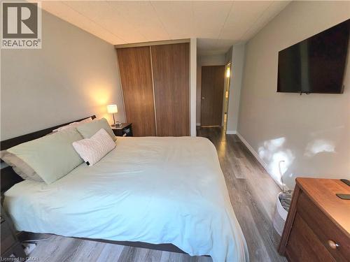 Bedroom featuring wood-finish flooring, light grey wall paint, and a built-in closet with sliding wood-finish doors - 24 Mooregate Crescent Unit# 103, Kitchener, ON - Indoor Photo Showing Bedroom