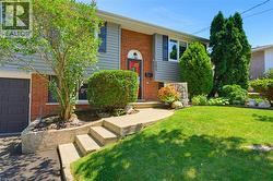 Brick and siding exterior featuring a red entry door, attached garage, concrete walkway, and a manicured lawn with mature trees - 