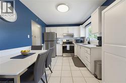 Open-concept kitchen and dining area featuring white cabinetry, tile flooring, and stainless steel appliances - 