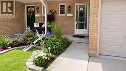 Brick exterior featuring a concrete walkway, landscaped garden beds with decorative stone edging, a paneled garage door, and a covered front porch - 