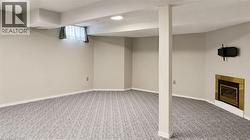 Spacious room featuring patterned gray carpet flooring, light neutral wall paint, a brass-framed fireplace, and a wall-mounted media bracket - 