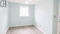 Interior room featuring light blue walls, wood-finish flooring, white baseboards, and a white window frame - 