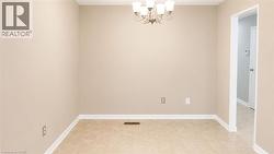 Neutral-toned walls with white baseboards frame a room featuring square tile flooring and a traditional five-light chandelier - 