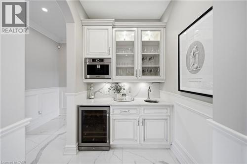 Built-in wet bar featuring white cabinetry, an integrated coffee system, a beverage cooler, and a single basin sink set in a light-toned countertop with a matching backsplash - 7009 Wellington Rd 34, Puslinch, ON - Indoor Photo Showing Other Room