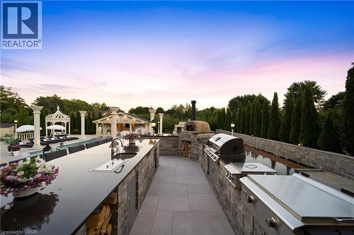 Outdoor kitchen featuring extensive countertop space, an integrated sink, built-in stainless steel appliances, a pizza oven, and stacked stone finishes - 7009 Wellington Rd 34, Puslinch, ON - Outdoor