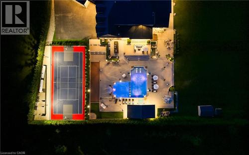 Expansive outdoor living area featuring a multi-sport court with perimeter lighting, a large illuminated swimming pool, extensive concrete patio space, and multiple shaded lounge areas - 7009 Wellington Rd 34, Puslinch, ON - 