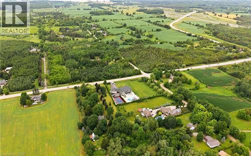 Aerial perspective showcasing expansive green landscapes, surrounding wooded areas, and a visible roadway - 7009 Wellington Rd 34, Puslinch, ON - Outdoor With View