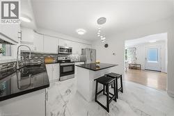 Kitchen featuring white cabinetry, black countertops, stainless steel appliances, and a mosaic tile backsplash - 