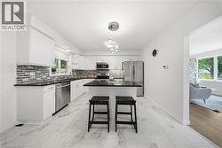 Modern kitchen featuring white cabinetry, stainless steel appliances, a center island with bar seating, a tile backsplash, and light-toned flooring - 