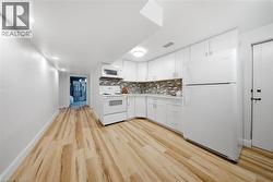 Kitchen area featuring white cabinetry, a mosaic tile backsplash, wood-finish flooring, recessed lighting, and a full suite of white appliances - 