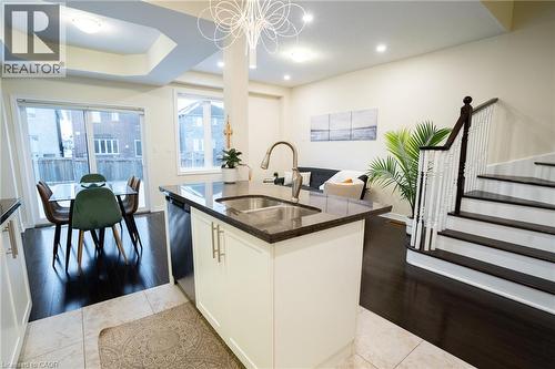 Kitchen island with granite countertop and stainless steel sink, dark wood-finish flooring, white staircase with dark wood handrail, recessed lighting, and patio door access to a fenced yard - 44 Medici Lane, Hamilton, ON - Indoor Photo Showing Kitchen With Double Sink With Upgraded Kitchen