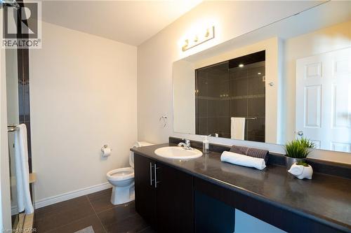 Contemporary bathroom featuring dark tile flooring, a spacious vanity with a dark countertop and integrated sink, a large wall-mounted mirror, and a glass-enclosed shower with dark tile surround - 44 Medici Lane, Hamilton, ON - Indoor Photo Showing Bathroom