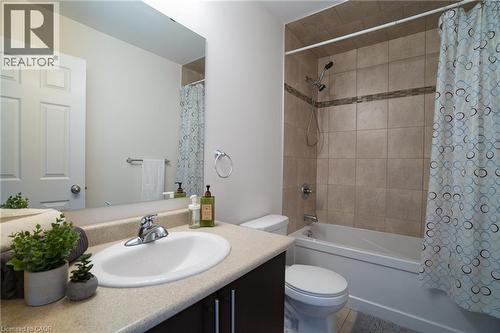 Bathroom featuring a full vanity with an integrated sink, a rectangular mirror, a toilet, and a combination shower/bathtub with tile surround and an accent tile band - 44 Medici Lane, Hamilton, ON - Indoor Photo Showing Bathroom