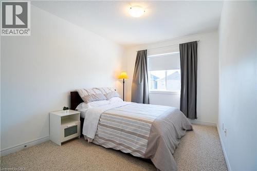 Bright room featuring a single window with a roller shade, carpet flooring, a flush-mount ceiling light fixture, and white painted walls - 44 Medici Lane, Hamilton, ON - Indoor Photo Showing Bedroom
