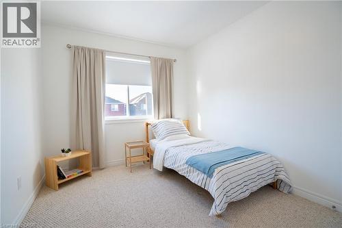 Carpeted room featuring a window with roller shade and drapes, white baseboards, and bright white walls - 44 Medici Lane, Hamilton, ON - Indoor Photo Showing Bedroom