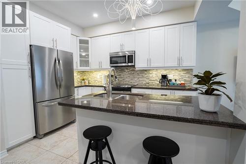 Modern kitchen featuring white cabinetry, stainless steel appliances, a breakfast bar with a dark countertop, and a textured tile backsplash - 44 Medici Lane, Hamilton, ON - Indoor Photo Showing Kitchen With Stainless Steel Kitchen With Double Sink With Upgraded Kitchen