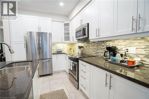 Modern kitchen featuring white cabinetry, stainless steel appliances, dark granite-style countertops, mosaic tile backsplash, and light-toned floor tiling - 44 Medici Lane, Hamilton, ON - Indoor Photo Showing Kitchen With Stainless Steel Kitchen With Double Sink With Upgraded Kitchen