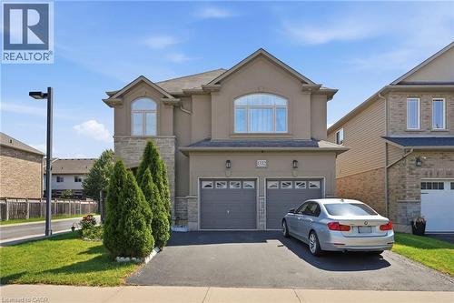 Stucco and stone facade home featuring a double-door garage, arched windows, manicured front lawn, and a paved driveway - 1332 Baseline Road, Stoney Creek, ON - Outdoor