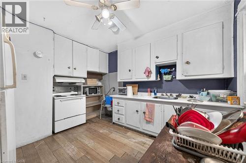 Kitchen featuring white cabinetry, wood-finish flooring, a white range with an overhead exhaust, and a ceiling fan with integrated lighting - 817 King Street E, Hamilton, ON 