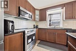 Kitchen featuring wood-finish cabinetry, dark countertops, white square tile backsplash, and stainless steel appliances including an oven range and microwave - 
